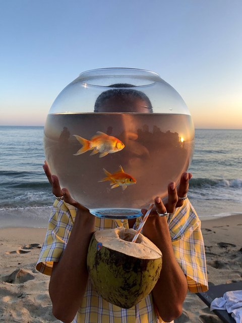 A fishbowl held like a face — original AI-generated fictional character